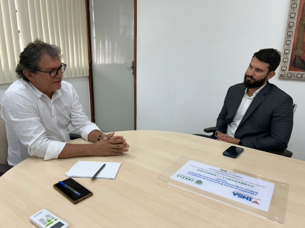 A imagem mostra o superintendente da Funetec, Rodrigo Barreto e o diretor do INSA, Etham Barbosa, sentados frente a frente em uma mesa redonda de madeira clara, em um ambiente que parece ser um escritório ou sala de reuniões. Etham está à esquerda ve
